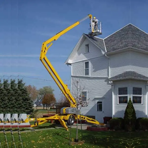 Yellow tow behind lift trimming trees near residential property